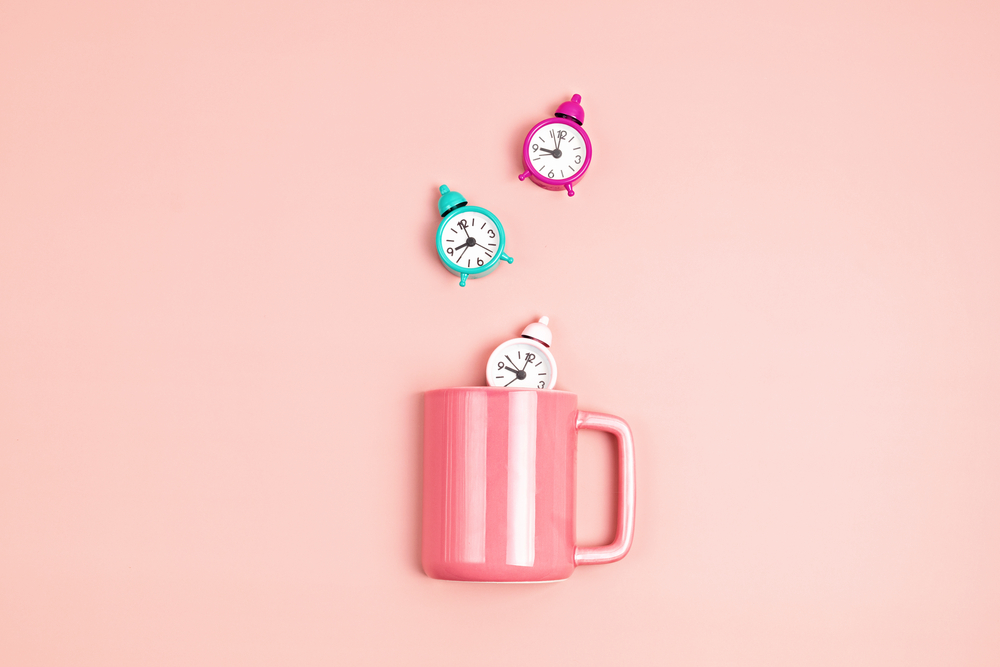 Pink cup with alarm clocks over pastel background. Morning, tea or coffee time, relaxation concept. Top view, flat lay, mockup
