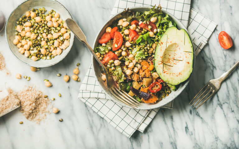 Vegan lunch bowl. Flat-lay of dinner with avocado, grains, beans, sprouts, greens and vegetables over marble background, top view. Clean eating, vegetarian, healthy diet food concept