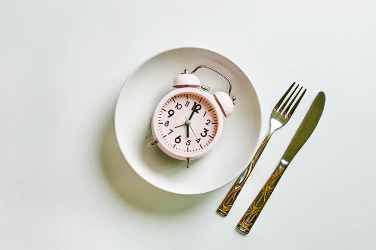Alarm clock on plate, spoon and fork on white background