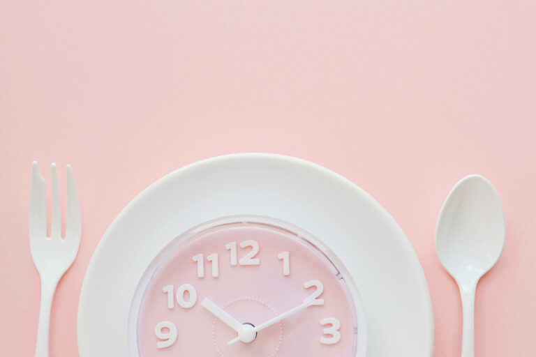 Pink clock on white plate with fork and spoon, Intermittent fasting concept, ketogenic diet, weight loss, skip meal