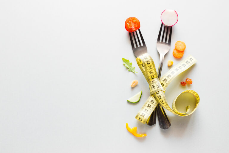 fresh vegetables on a fork and measuring tape on a white background with place for text concept healthy diet for weight loss